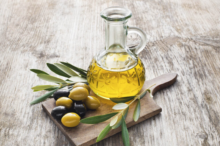 Brocca con olio extravergine d'oliva su ramoscello d'ulivo e olive verdi e nere su tagliere in legno