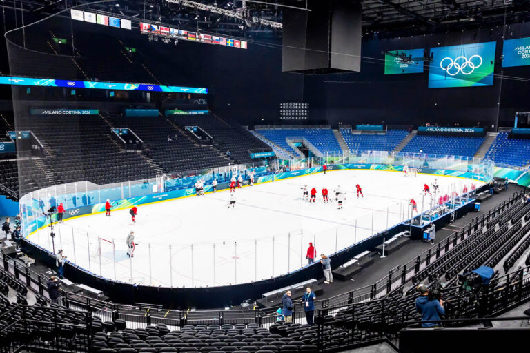 Arena del PalaItalia Santa Giulia a Milano durante i preparativi per le Paralimpiadi Milano Cortina 2026, con pista da hockey su ghiaccio, atleti in allenamento e tribune illuminate con il logo olimpico