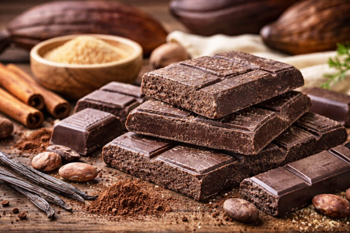 Tavolette di cioccolato di Modica IGP con tipica consistenza granulosa accanto a fave di cacao, zucchero e spezie